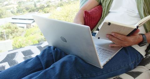 Woman working on laptop and taking notes on balcony with city view for remote learning