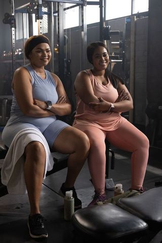 African american friends sitting wearing matching workout gear in gym with barbells