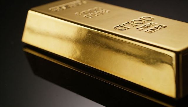 Polished gold bullion bar reflecting on glossy black surface with embossed hallmarks