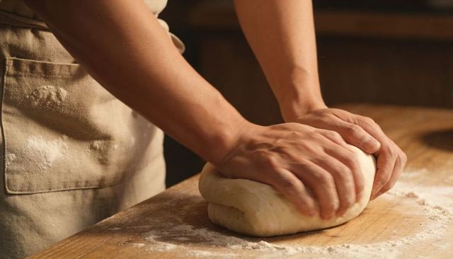 Artisan Hands Kneading Dough on Wooden Board with Scattered Flour and Apron Pocket