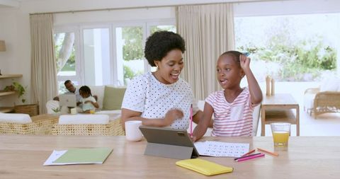 Mother and Daughter Using Tablet for Homework, Family in Background