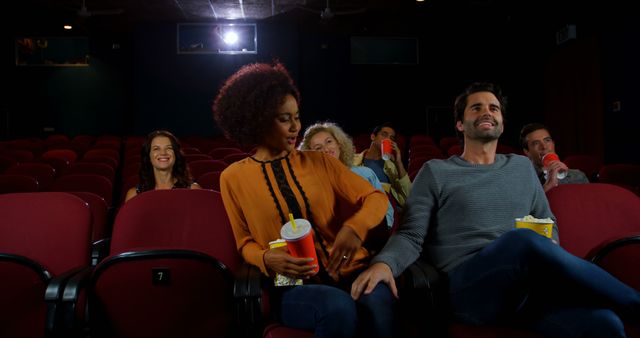Group of friends sitting in movie theater seats, holding popcorn and drinks, watching a film and enjoying the experience. Ideal for use in advertisements for cinemas, social invitations to movie nights, and articles related to entertainment, movies, and leisure activities.