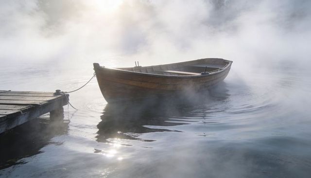 Misty morning rowboat floating beside weathered dock at sunrise