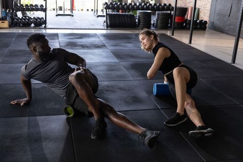 Diverse fitness partners using foam rollers for mobility and recovery in functional gym