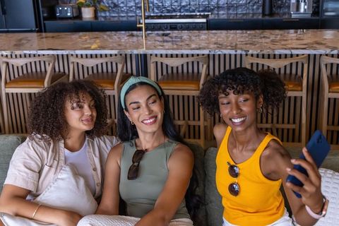 Diverse friends taking selfie on modern kitchen sofa, smiling and relaxing together