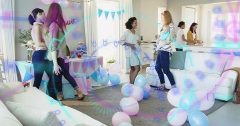 Women celebrating baby shower at home holding infant, pastel balloons, cupcakes and gifts