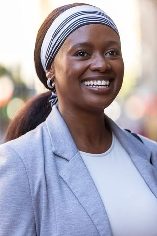 Confident african woman smiling in city headshot wearing striped headband, blazer, hoop earrings