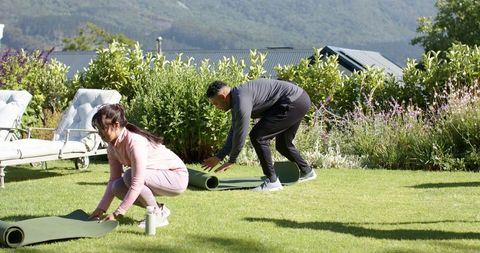 African american friends unrolling yoga mats on backyard lawn for outdoor fitness session