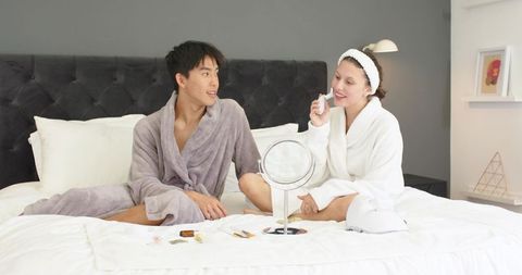 Couple enjoying skincare routine on bed using facial device and mirror