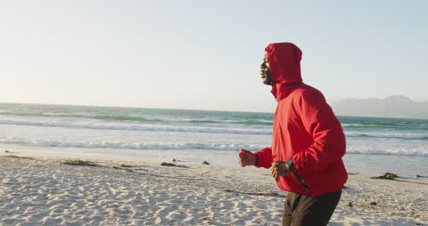 Man Running on Beach in Red Hoodie at Sunrise