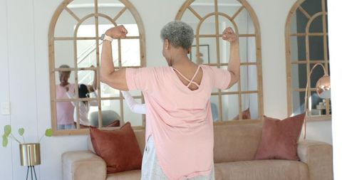 African american senior woman flexing with young family member in cozy living room mirrors