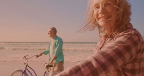 Joyful senior couple cycling on beach, celebrating retirement and togetherness