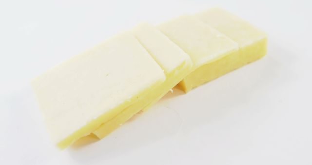Close-up view of several slices of fresh block cheese arranged on a plain white background. The clean and simple presentation focuses on the texture and color of the cheese. Ideal for use in culinary articles, dairy product advertisements, recipe illustrations, or food blogs. This image emphasizes freshness and quality, appealing to those interested in cooking and healthy eating.