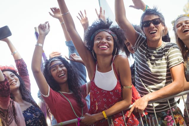 Group of friends having fun at a music festival, raising their hands and smiling. Ideal for promoting music events, festivals, youth culture, and social gatherings. Perfect for use in advertisements, event promotions, and social media campaigns highlighting fun and excitement.