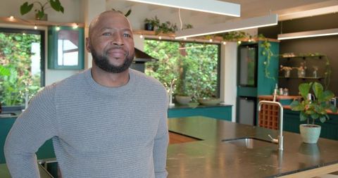 Middle-aged african american man standing by modern kitchen island with green plants