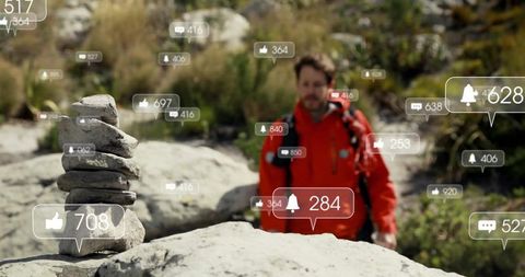 Hiker in red jacket contemplating digital interaction amidst rocks and nature