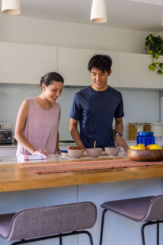 Young diverse couple preparing healthy breakfast on modern kitchen island with bowls