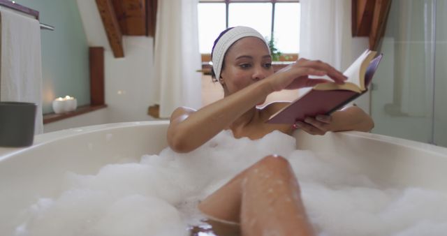 Woman enjoys peaceful bubble bath while reading a book in a serene bathroom setting. This image ideal for promoting self-care routines, leisure activities, bath products, relaxation techniques, and peaceful home environments. Perfect for wellness blogs, lifestyle magazines, and spa advertisements.