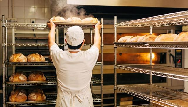 Baker placing steaming artisan sourdough loaves on wire racks near glowing ovens