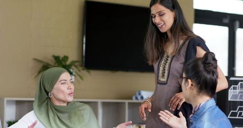Diverse women leading collaborative meeting in modern office with headscarf and team discussion