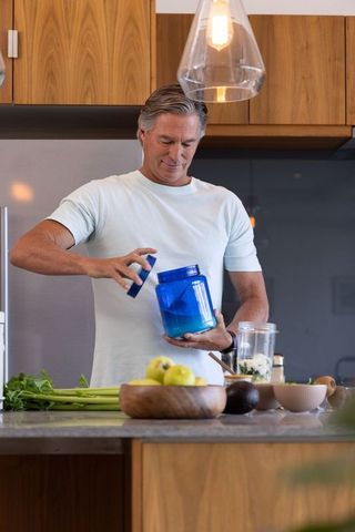 Mature man preparing smoothie at modern kitchen island with wooden cabinets