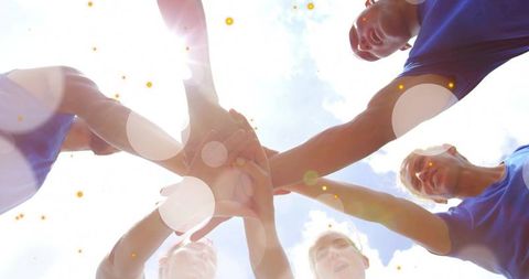 Forming team huddle: six athletes joining hands under sun with lens flare