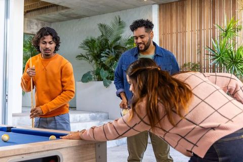 Friends playing pool on modern patio enjoying casual outdoor billiards and social fun