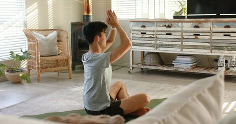 Asian man practicing meditation and yoga at home on green mat in sunlit living room