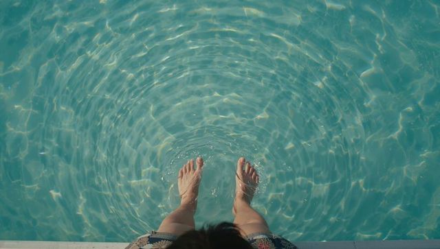 Dipping feet in turquoise pool water creating concentric ripples and sunlit reflections