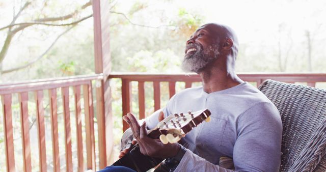 Happy senior african american man spending time in log cabin, playing guitar on balcony - Download Free Stock Photos Pikwizard.com