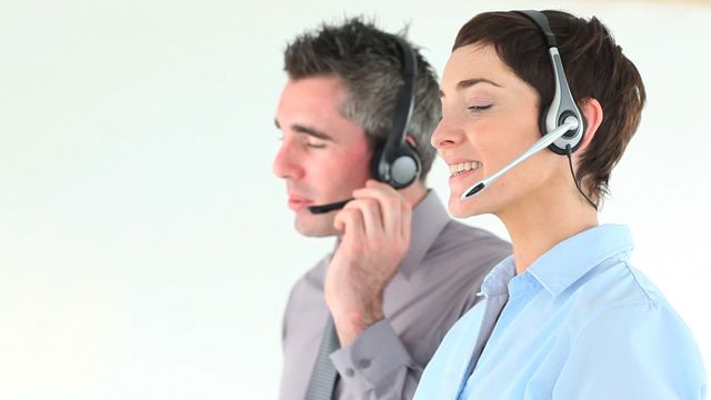 A man and woman wearing headsets inside a modern office environment, engaging in a professional phone conversation. This setting is ideal for illustrating concepts around corporate communication, teamwork, and efficient customer service operations. Useful for marketing materials, workplace training guides,_service automation brochures, and any content focused on enhancing business office infrastructures.