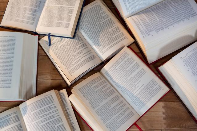 This image shows multiple open books spread out on a wooden table. It can be used for educational content, library promotions, book clubs, or any material related to reading and literature. Ideal for illustrating concepts of study, knowledge, and academic research.