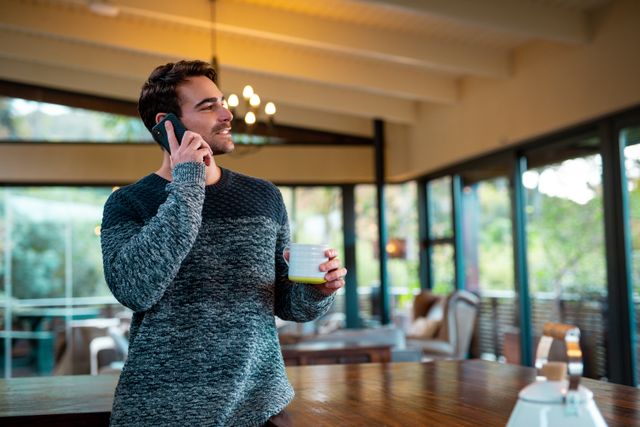 Caucasian man holding mug and talking by smartphone. enjoying free time in luxury rural home.