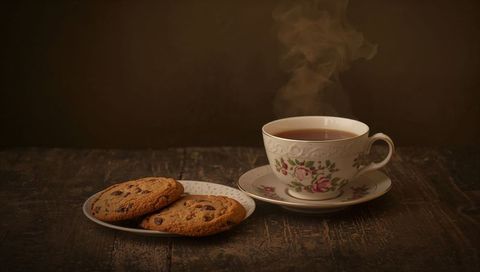 Steaming vintage teacup with chocolate chip cookies on rustic wooden table