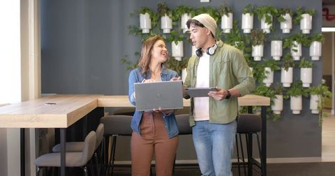 Young professionals collaborating with laptop and tablet in modern green coworking space