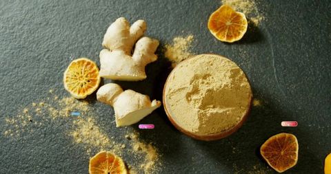 Ginger Powder with Fresh Root and Dried Citrus on Stone Surface