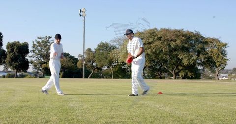 Cricket players placing cones for fielding drill on sunny outfield