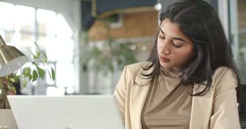 Indian businesswoman working on laptop in modern coworking office, focused and productive