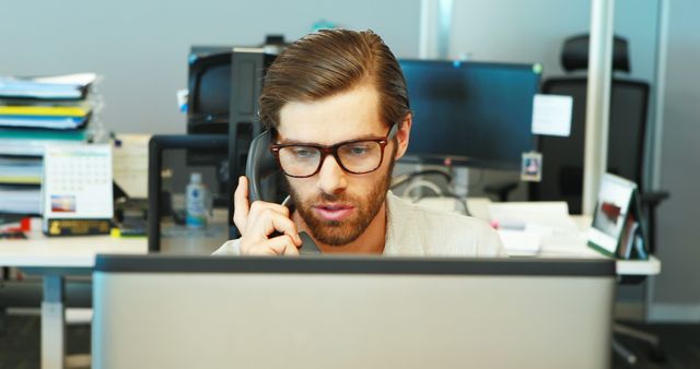 Focused Young Professional Man Talking on Phone at Office Desk - Download Free Stock Photos Pikwizard.com