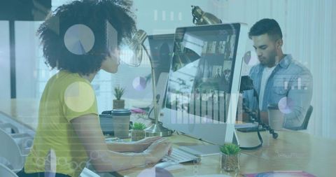 Curly-haired woman typing at desktop while colleague films content in modern coworking space