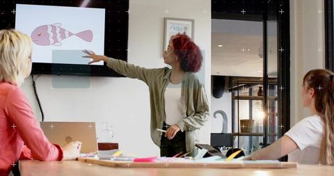 Presenter pointing at screen with pink fish illustration while team brainstorming at meeting table