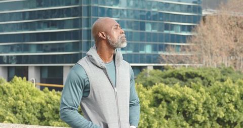 African American senior man gazing upward on urban rooftop with modern glass architecture