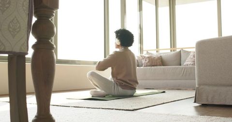 Mid-age man sitting cross-legged meditating with headphones in minimalist living room