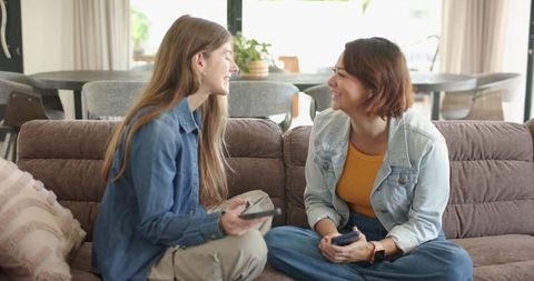 Young diverse friends smiling and using smartphones on cozy open-plan living room sofa