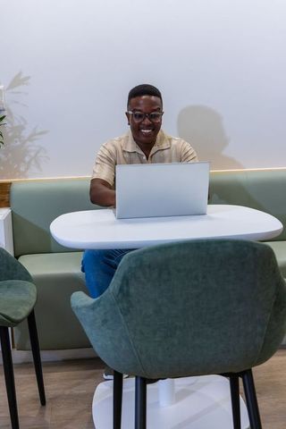 Smiling man working on laptop in modern coworking lounge wearing casual short-sleeve shirt
