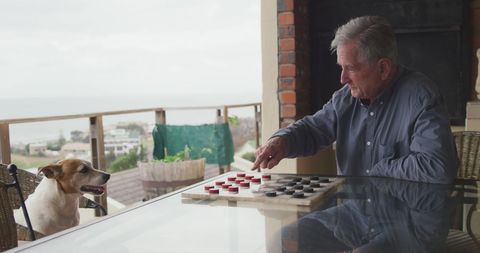 Senior Man Enjoying Game of Checkers with Dog Outdoors