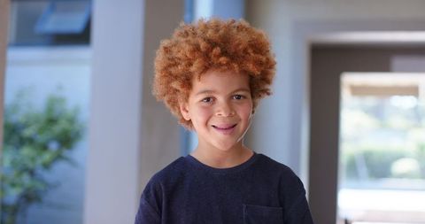 Smiling african american boy with red curly hair standing in bright doorway portrait