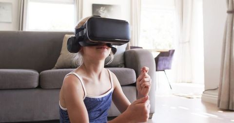 Teenage girl exploring virtual reality at home wearing black VR headset sitting on floor