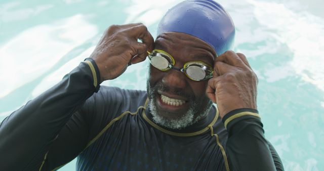 Senior Black man adjusting swim goggles while standing in pool wearing swim cap. The image highlights athletic activity, fitness, and healthy lifestyle of elderly individuals. Ideal for advertising sports equipment, fitness programs for seniors, health and wellness campaigns, and active lifestyle promotions.