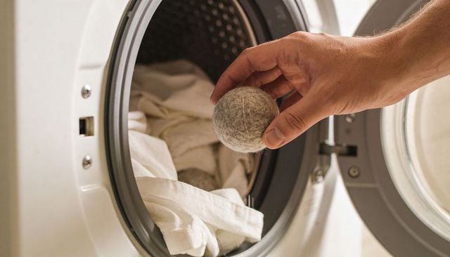 Hand placing gray wool dryer ball into front-load washer drum softening white linens
